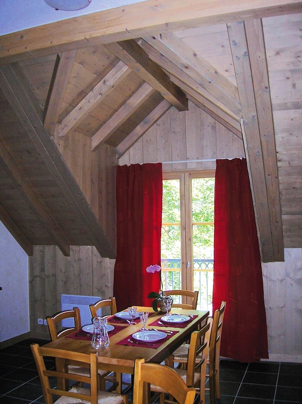 Comedor con una mesa de madera dispuesta para cuatro, cortinas rojas y vistas al exterior con vegetación.