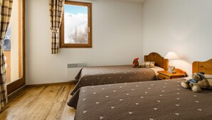 Ein Schlafzimmer mit zwei Betten, einem Fenster mit Vorhängen, einem Nachttisch mit Lampe und einem Teddybären.