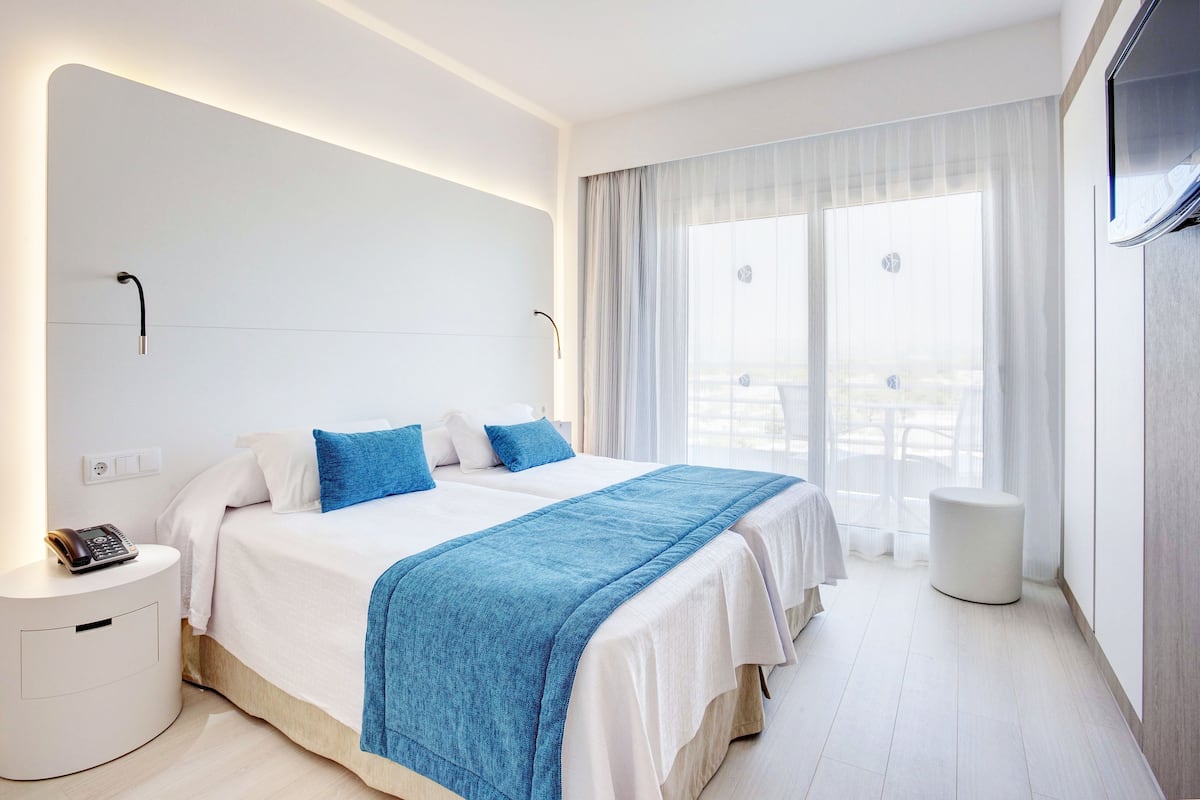 Ett modernt hotellrum med en stor säng, ett nattduksbord med en telefon och utsikt över omgivningarna genom tunna gardiner.