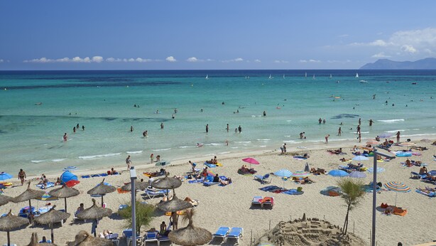 A beach with clear turquoise water, people swimming, and beachgoers relaxing under umbrellas. - Grupotel Farrutx (Santa Margalida)