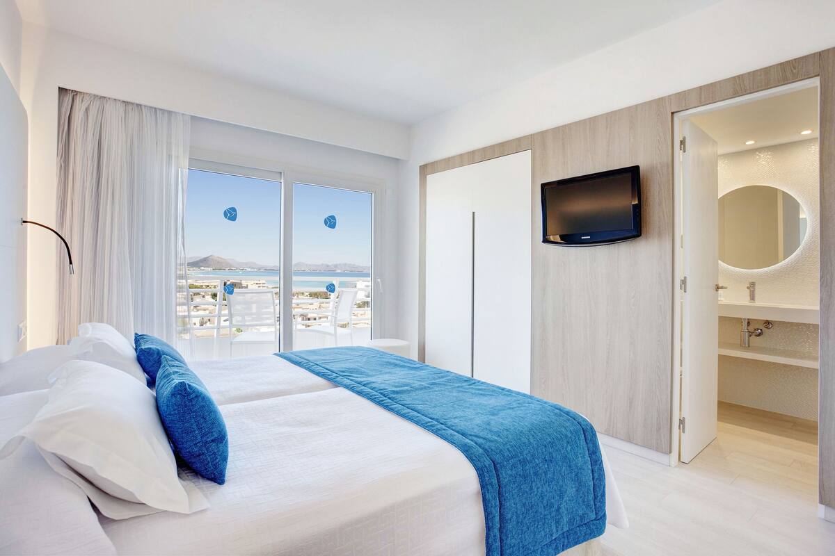 Ett modernt hotellrum med en stor säng, en tv som är monterad på väggen och utsikt över staden genom fönstret.