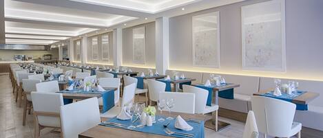 Un restaurante moderno con mesas largas, sillas blancas y manteles azules.