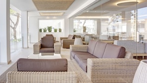 A modern living room with wicker furniture, large windows, and a glass wall. - Grupotel Farrutx (Santa Margalida)