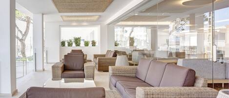 A modern living room with wicker furniture, large windows, and a glass wall.
