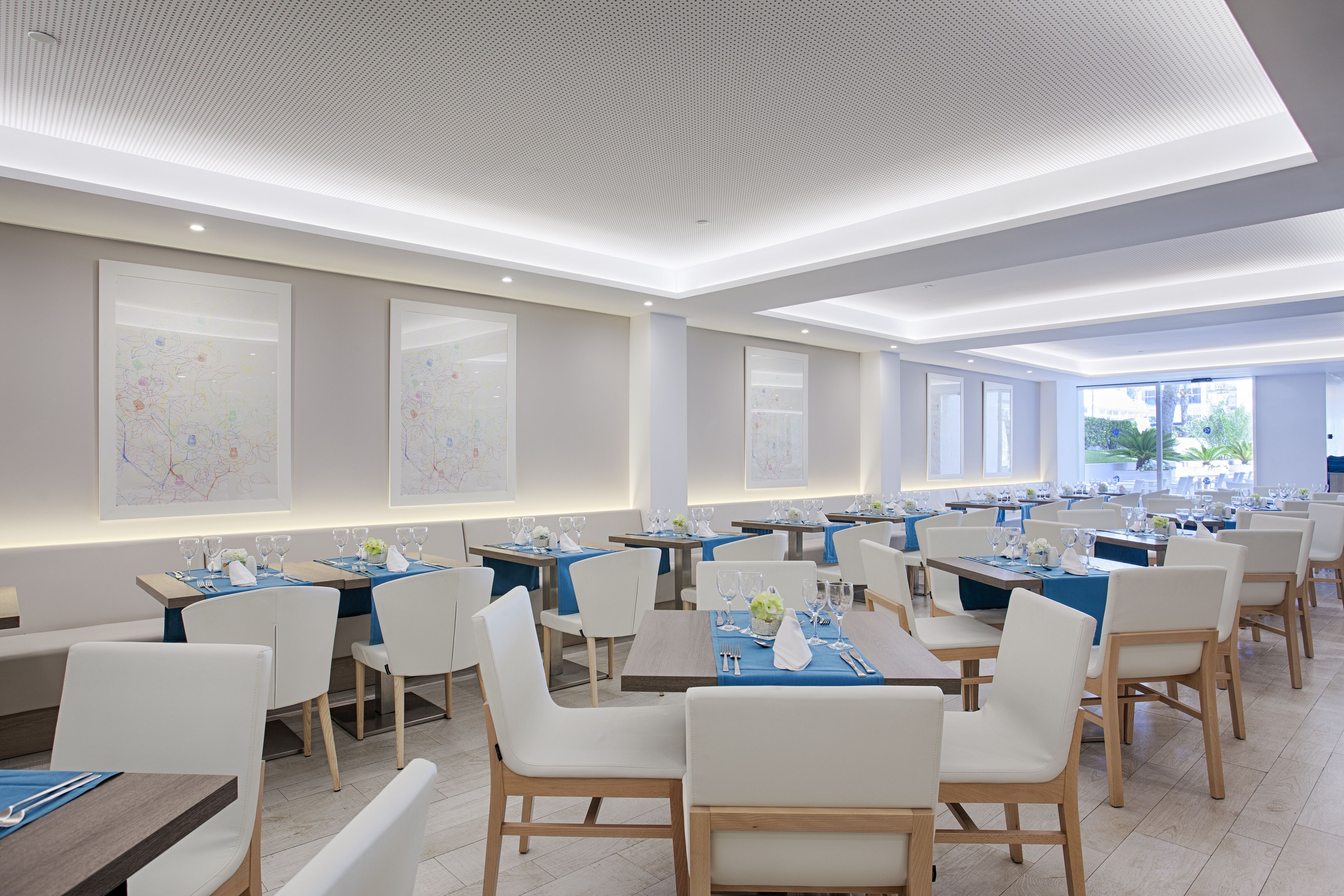 A spacious dining area with multiple tables and chairs, featuring a modern ceiling design and large windows allowing natural light.