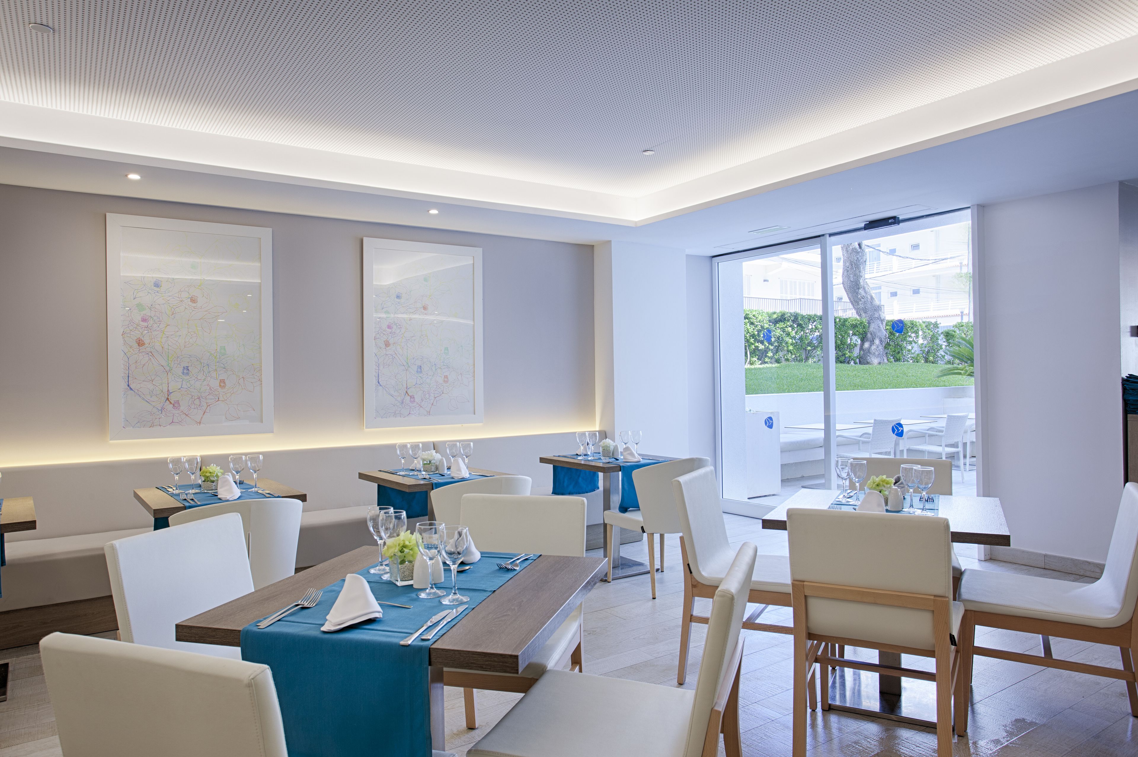A modern dining area with tables set for four, featuring blue tablecloths and white chairs.