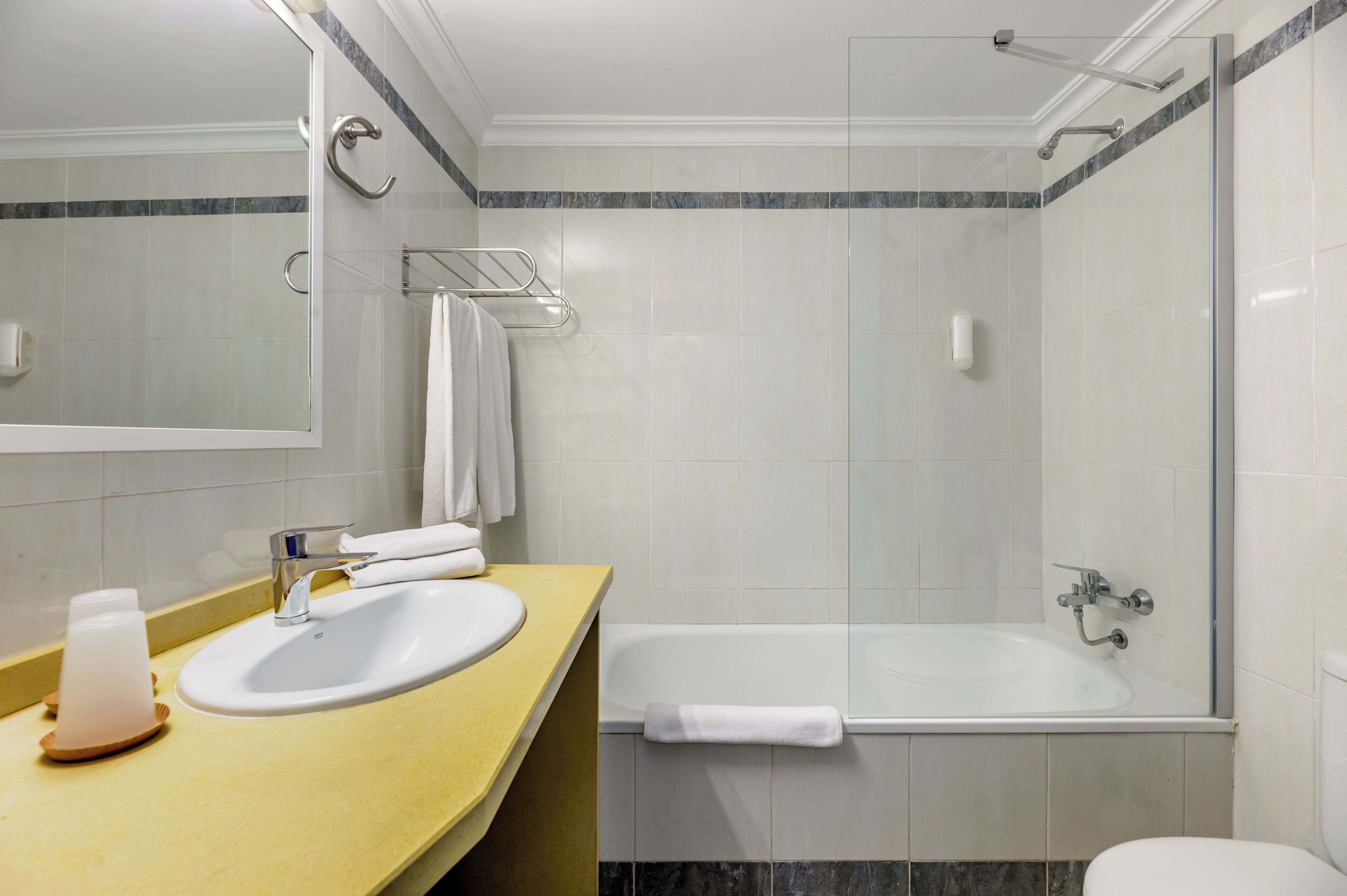 Un baño con lavamanos, espejo, toallero y ducha.