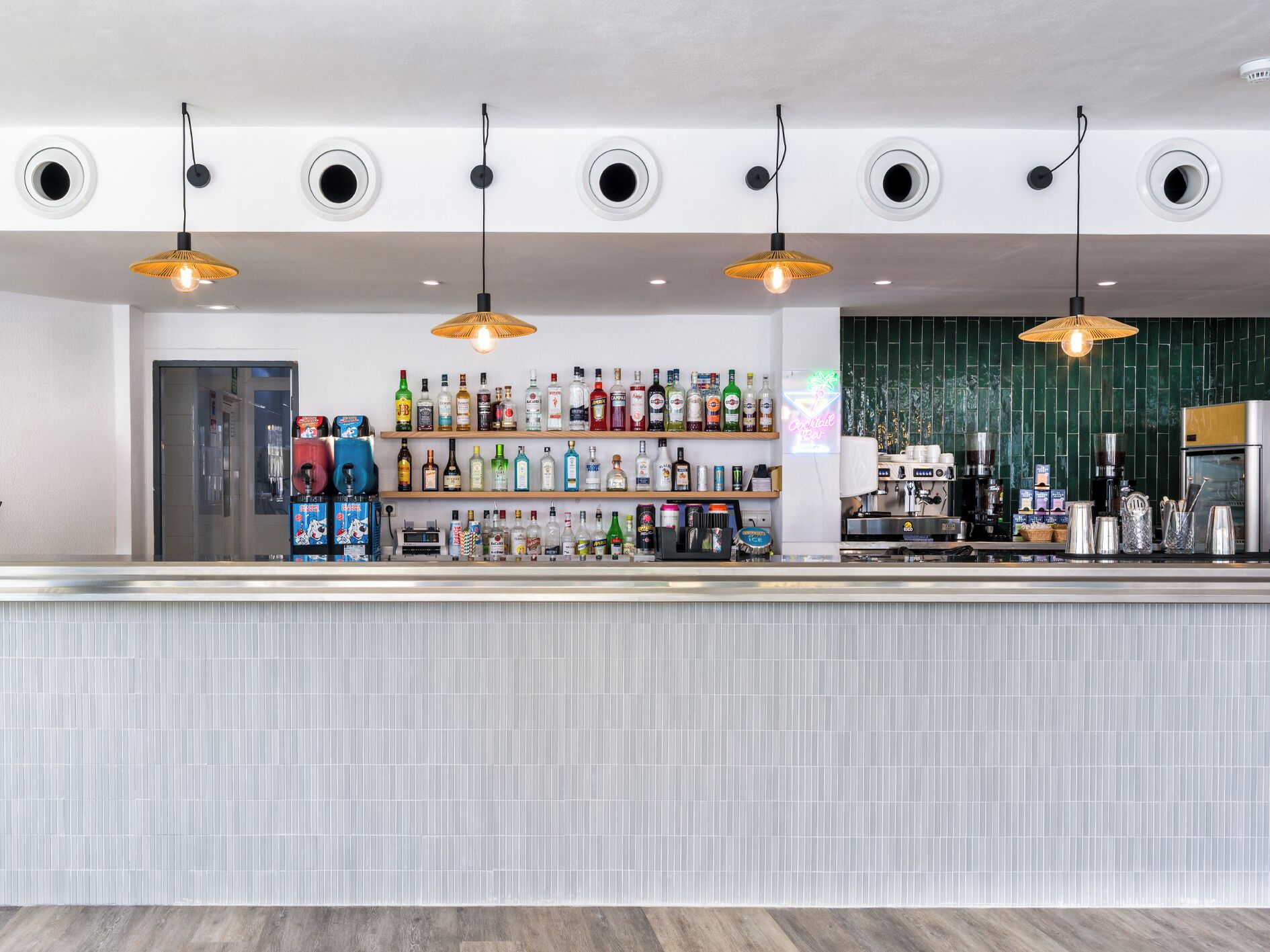 A bar area with a counter, shelves of various bottles, and hanging pendant lights.