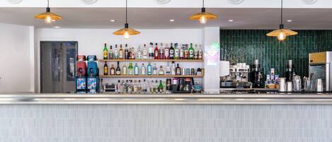 A bar area with a counter, shelves of various bottles, and hanging pendant lights.
