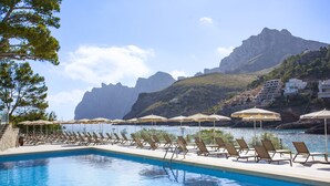 En pool med liggestole og parasoller, et bjergrigt baggrund og en klar himmel.