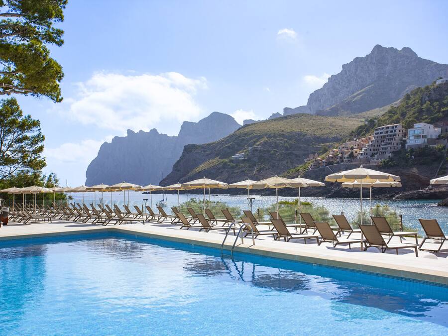 Une piscine bordée de chaises longues et d’ombrelles, un paysage montagneux en toile de fond et un ciel dégagé.