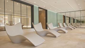 A row of modern, white lounge chairs in a spacious, well-lit indoor area with large windows and a tiled floor.