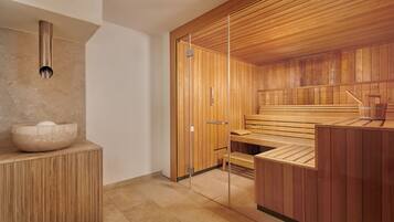 A sauna room with wooden benches, a stone basin, and a glass partition.