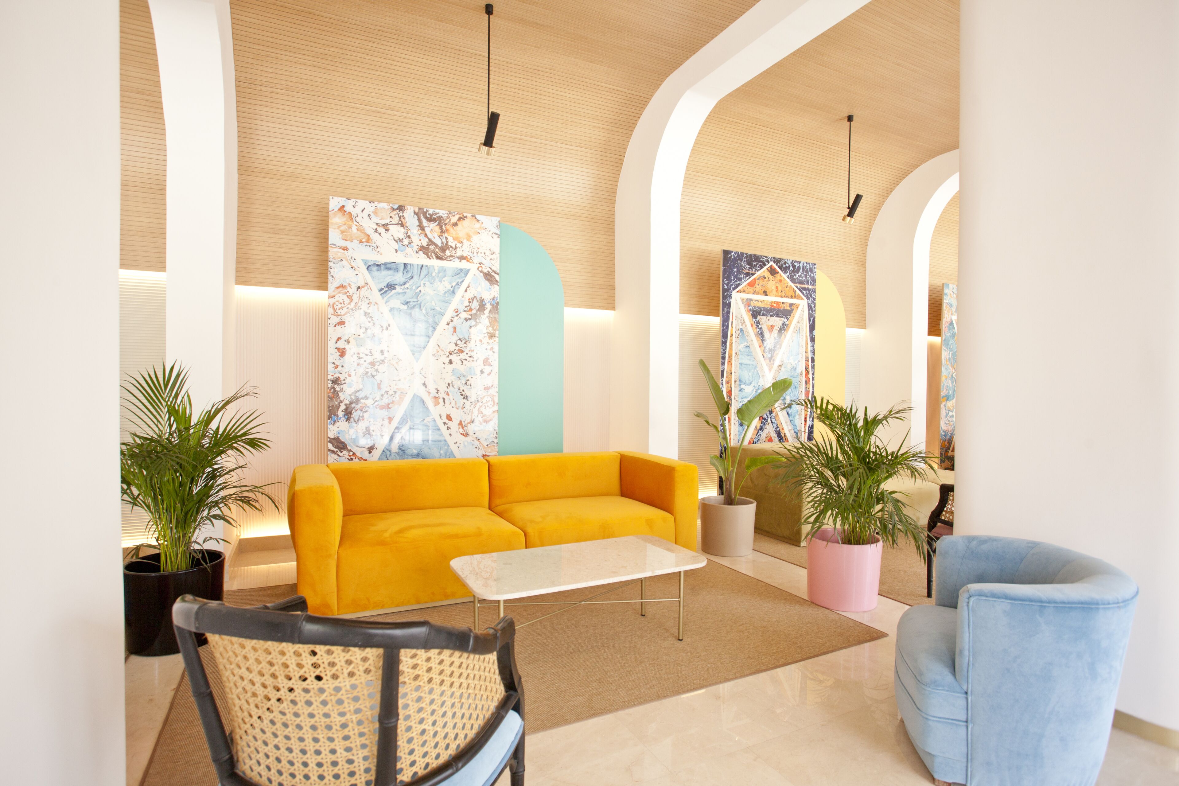 Un hall moderno con un sofá amarillo, un sillón azul y dos plantas en macetas.