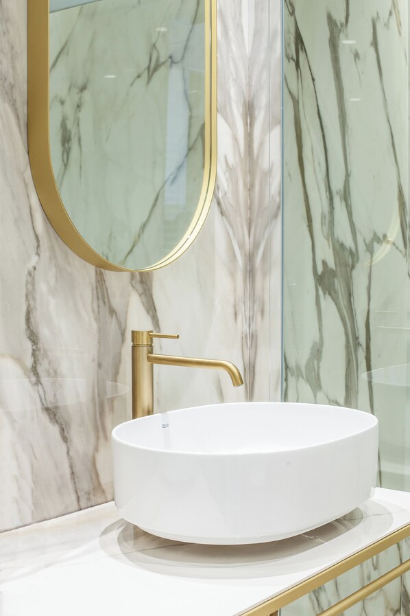 Un baño con lavamanos blanco, grifo dorado y espejo con marco dorado.