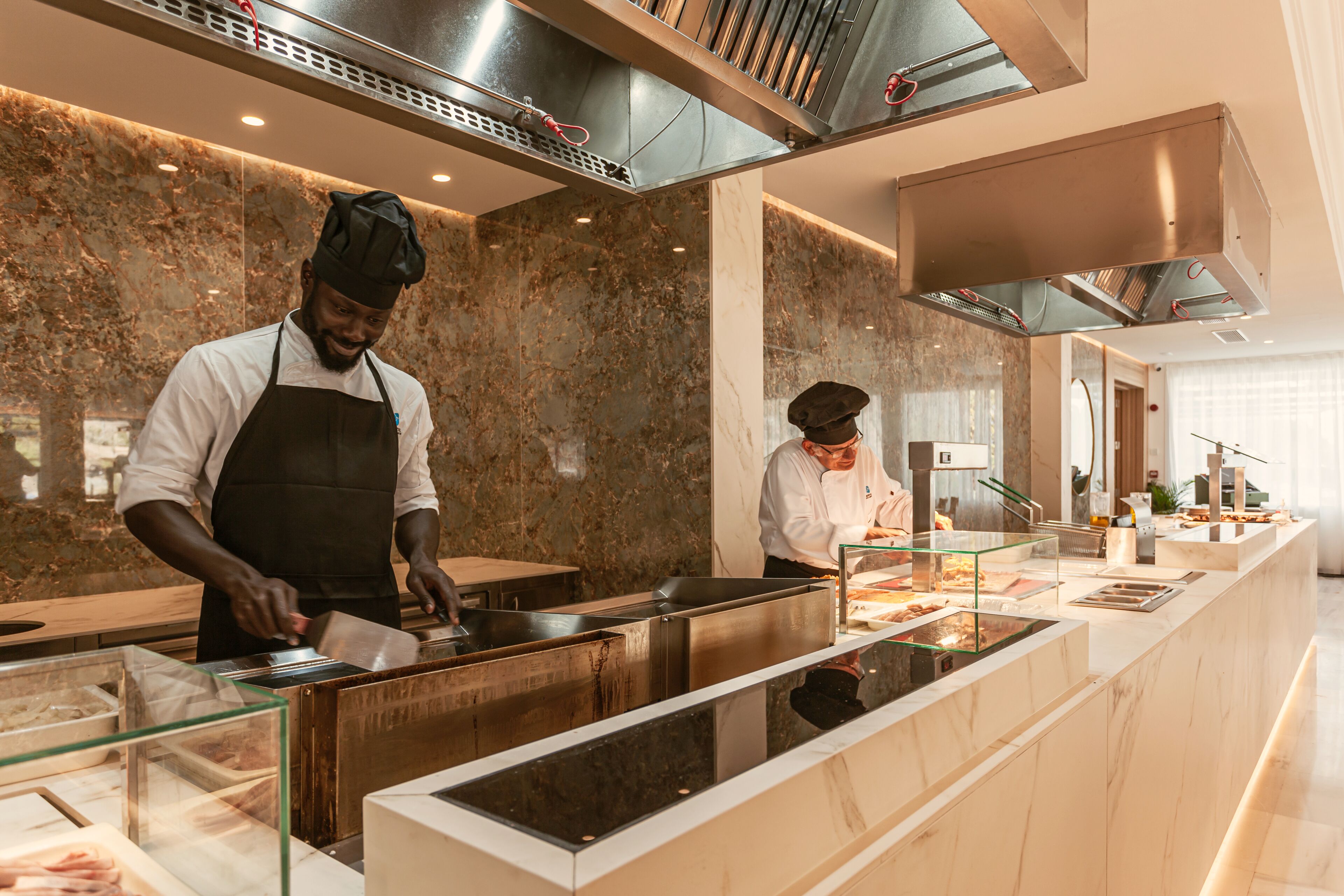 A modern kitchen with marble countertops, stainless steel appliances, and a glass display case.