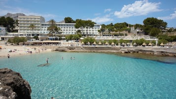 Un hotel costero con varios pisos, una zona de playa con sombrillas y agua turquesa cristalina.
