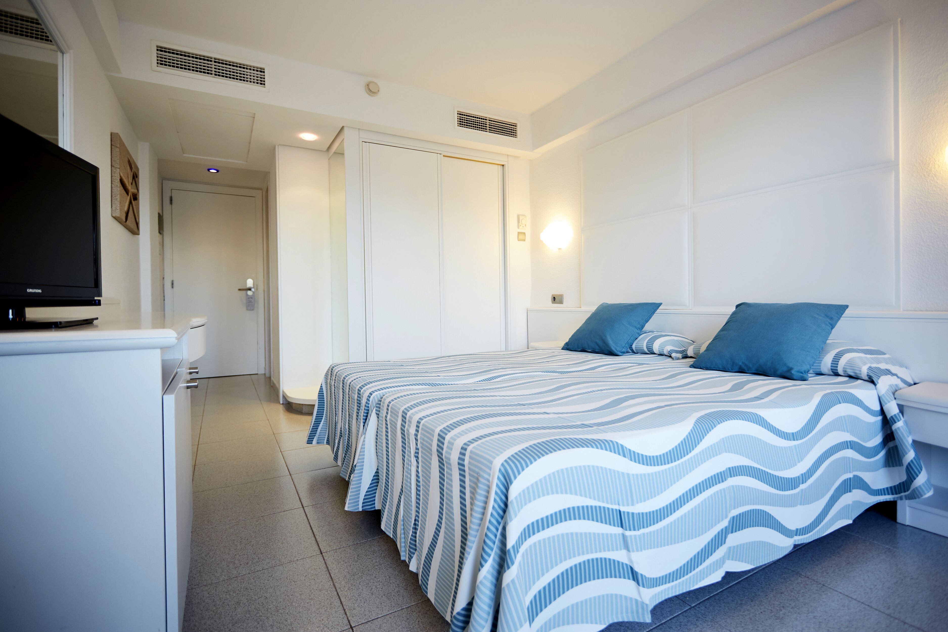 Un dormitorio con cama, televisor y un armario blanco.