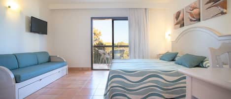 Un dormitorio con cama, sofá, televisor y balcón con mesa y sillas.