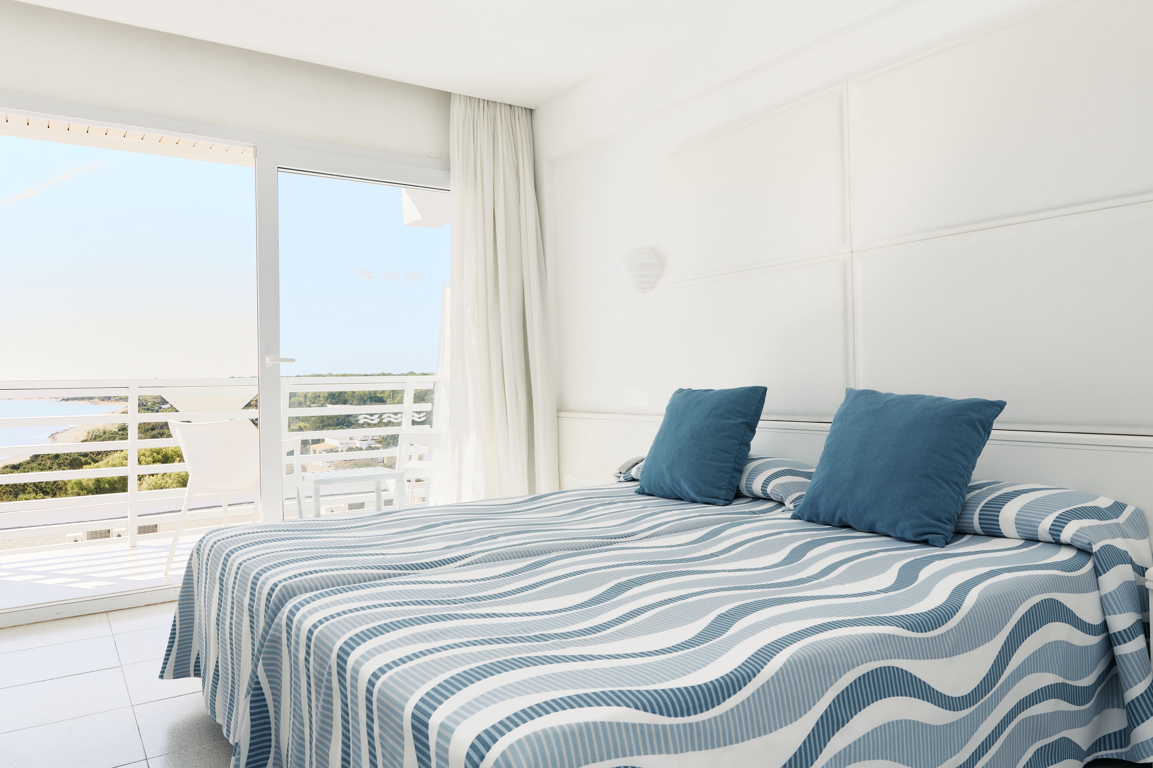 A bedroom with a large bed, two pillows, a window with curtains, and a view of the outdoors.