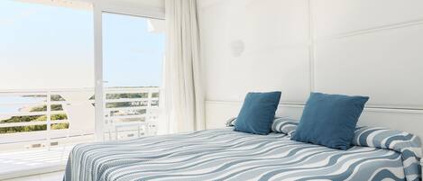 A bedroom with a large bed, two pillows, a window with curtains, and a view of the outdoors.