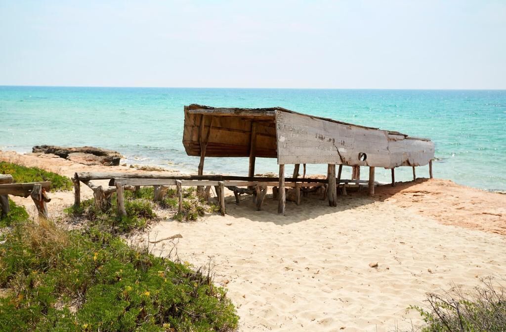 A wooden boat on a sandy beach with the ocean in the background.