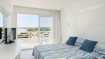 A bedroom with a bed, a TV, and a balcony with a view of the sea.