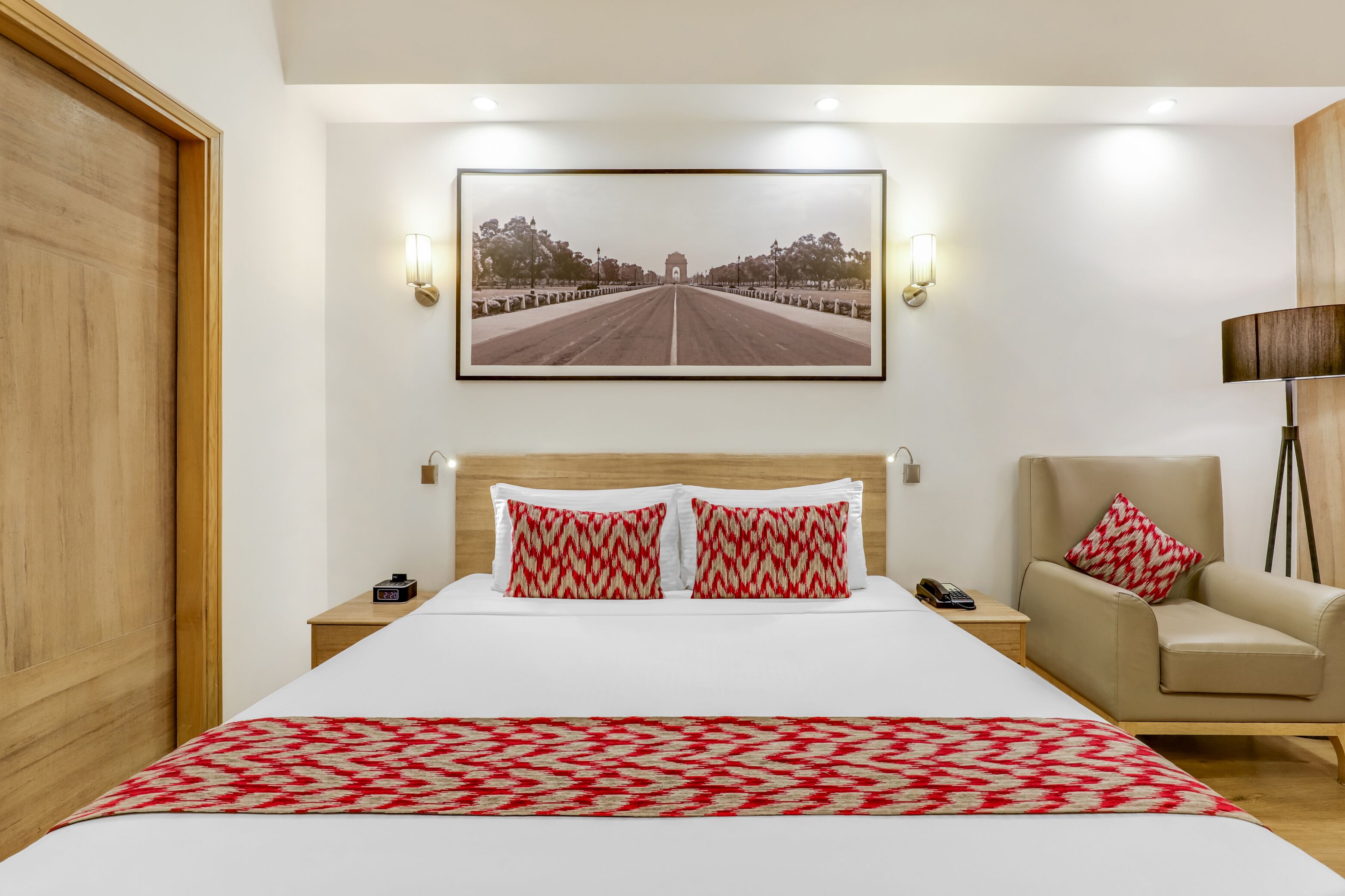 Ein Hotelzimmer mit einem großen Bett, zwei Nachttischen, einem Sessel, einer Lampe und einem gerahmten Bild an der Wand.