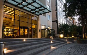 A modern hotel entrance with a glass facade, outdoor seating area, and a staircase leading to the entrance. - Lemon Tree Premier City Center Gurugram (Gurugram)