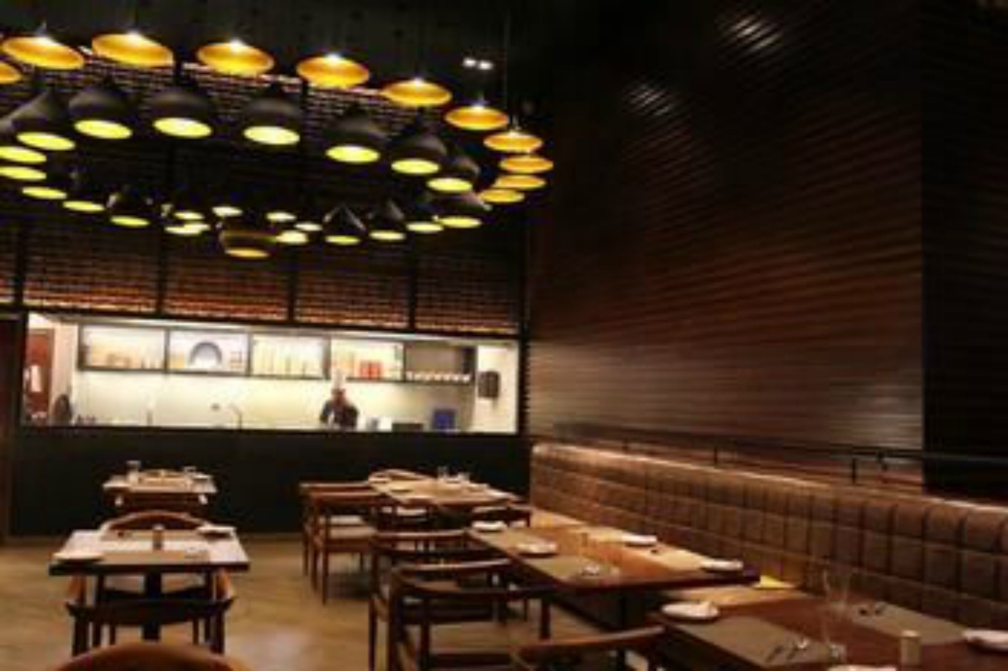 A restaurant interior with multiple tables and booths, a brick wall, and pendant lighting.