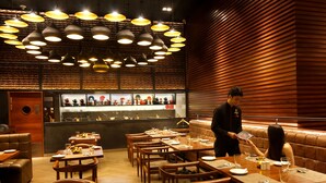 A restaurant with wooden furniture, pendant lighting, and a bar area. - Lemon Tree Premier City Center Gurugram (Gurugram)