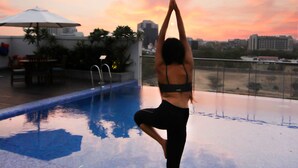 A person performing a yoga pose on a rooftop terrace with a pool and cityscape view. - Lemon Tree Premier City Center Gurugram (Gurugram)