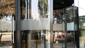 A revolving door with glass panels, a circular floor design, and a reflection of trees and cars. - Lemon Tree Premier City Center Gurugram (Gurugram)