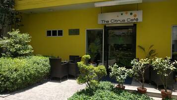 Café Citrus com mesas ao ar livre, plantas em vasos e um aviso de 'Área Proibido Fumar'.
