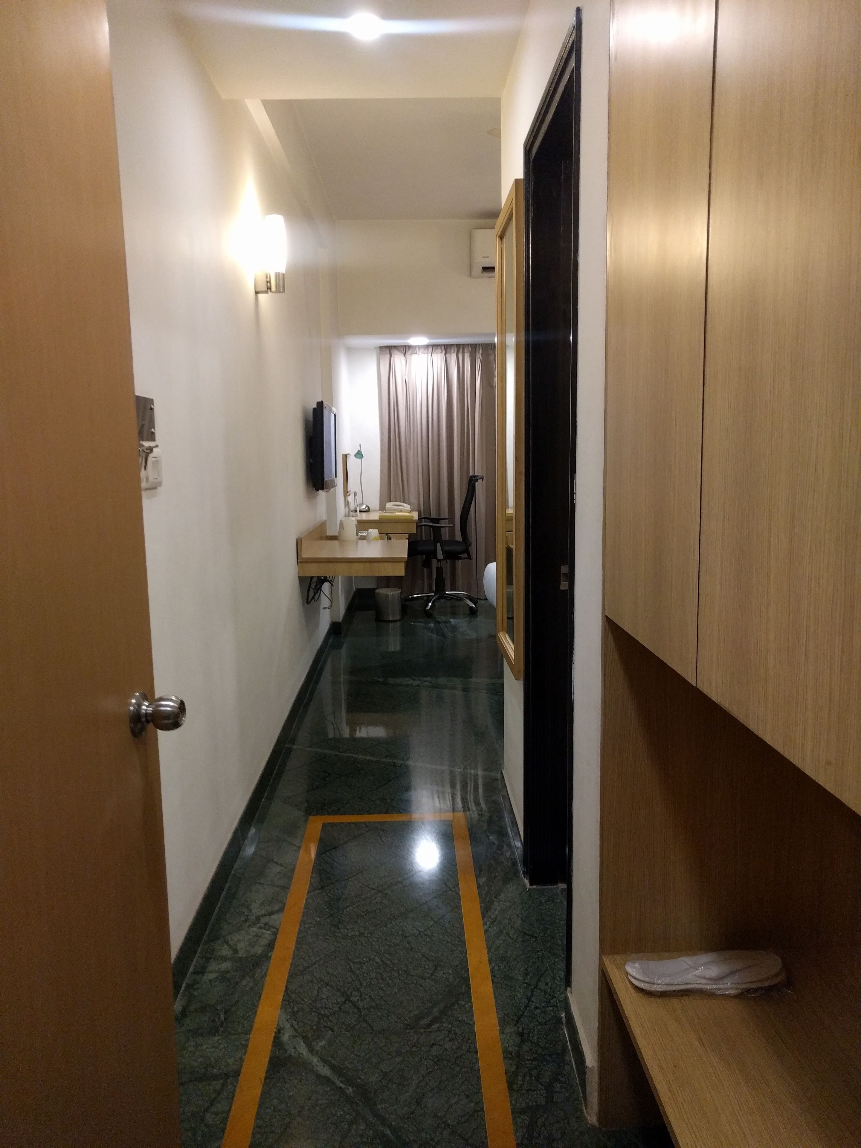 Een hotelgang met een houten deur, een bureau met telefoon, een stoel en een aan de muur bevestigde televisie.