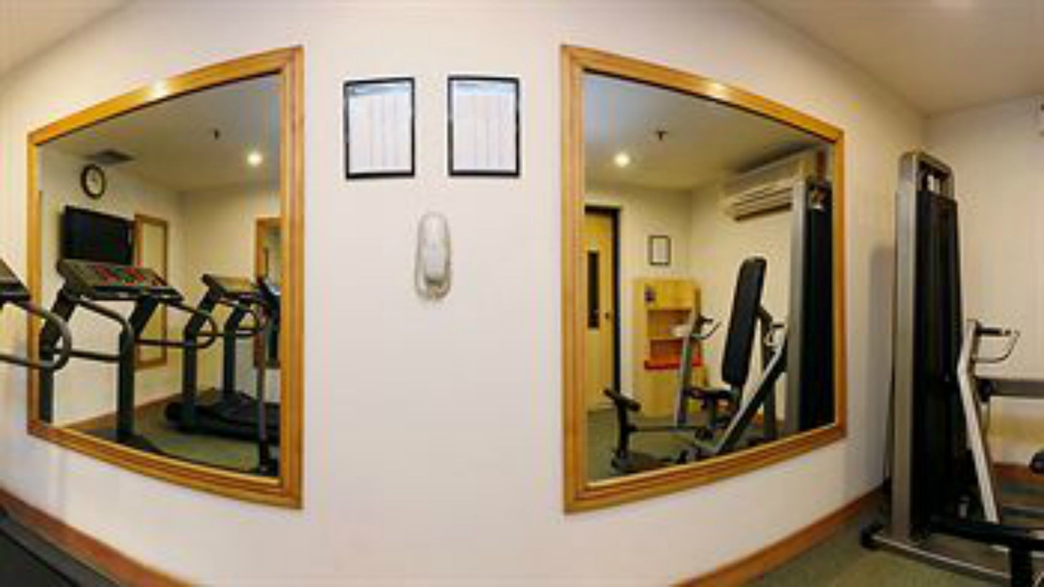 Un gimnasio con equipo de ejercicio, una cinta de correr y un espejo grande.
