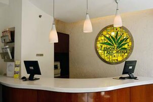 Un mostrador de recepción con dos monitores de computadora, un adorno circular en la pared y lámparas colgantes.