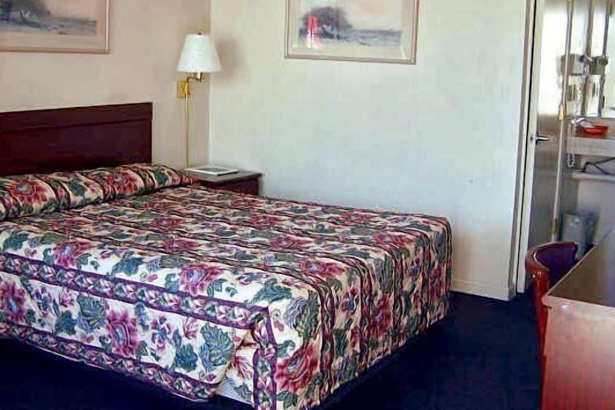 A hotel room with a bed, a nightstand, a lamp, and two framed pictures on the wall.