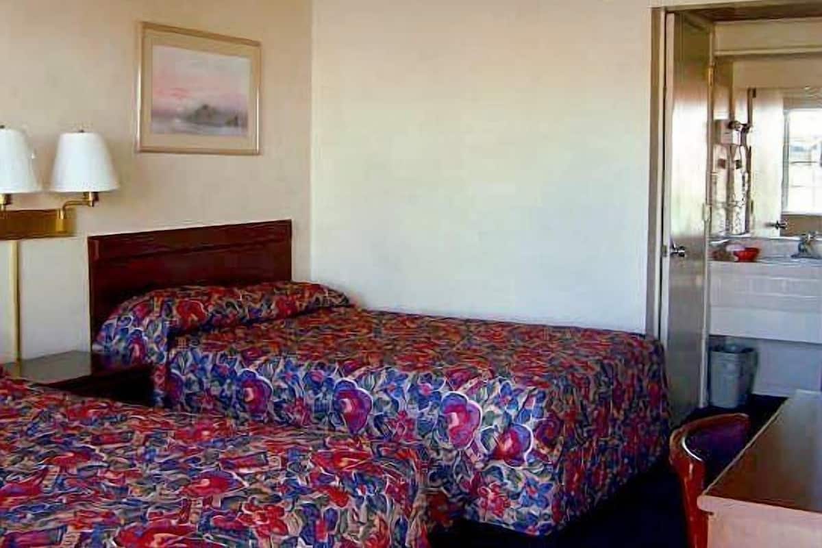 A hotel room with two beds, a desk, a chair, a lamp, and a painting on the wall.