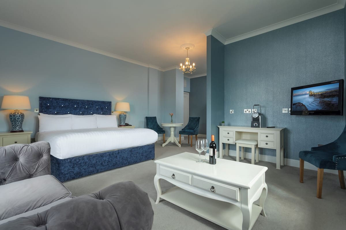 A hotel room with a large bed, a white desk, a TV, and a chandelier.
