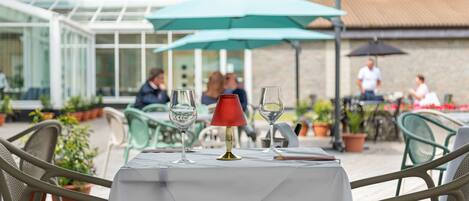 Un área de comedor al aire libre con una mesa preparada para dos personas, rodeada de sillas.