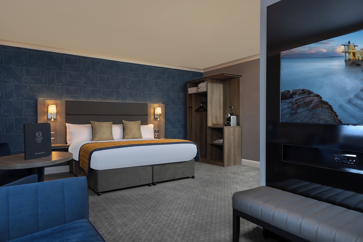 A hotel room with a large bed, a seating area, a TV, and a wardrobe.