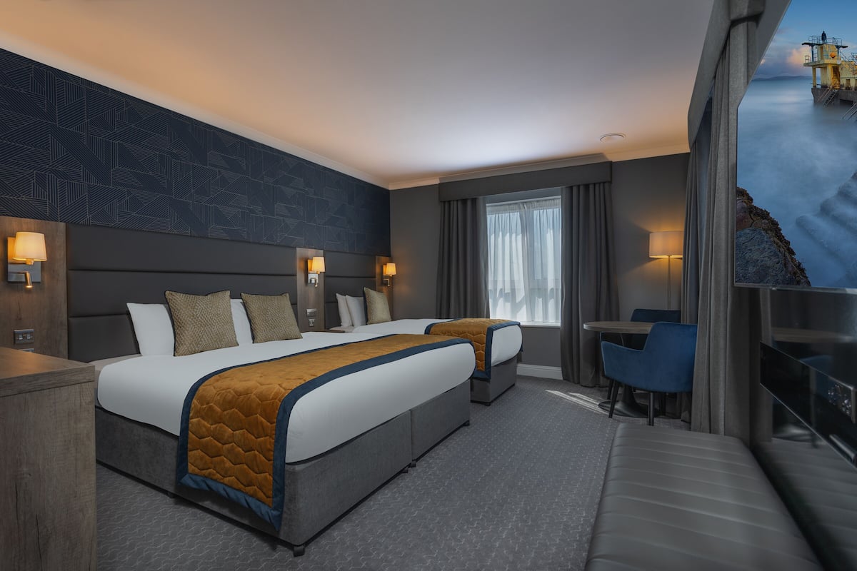 A modern hotel room with a large bed, a desk, and a view of a coastal landscape.