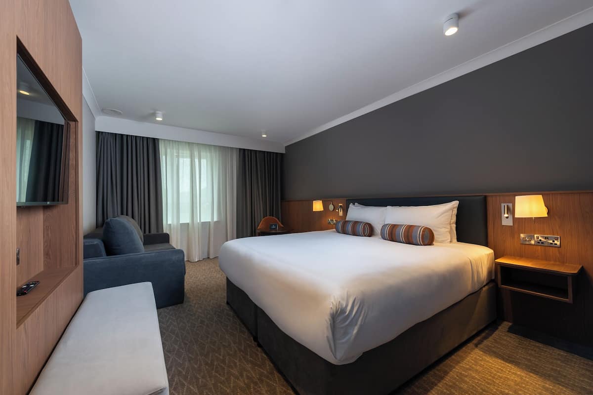 A hotel room with a large bed, a sofa, a TV, and a desk.