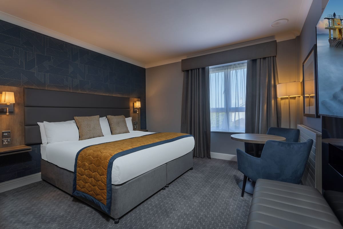 A hotel room with a large bed, a desk, a chair, and a small table.