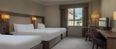 Habitación de hotel con dos camas, un escritorio, una silla, un televisor y una ventana con vistas a edificios.
