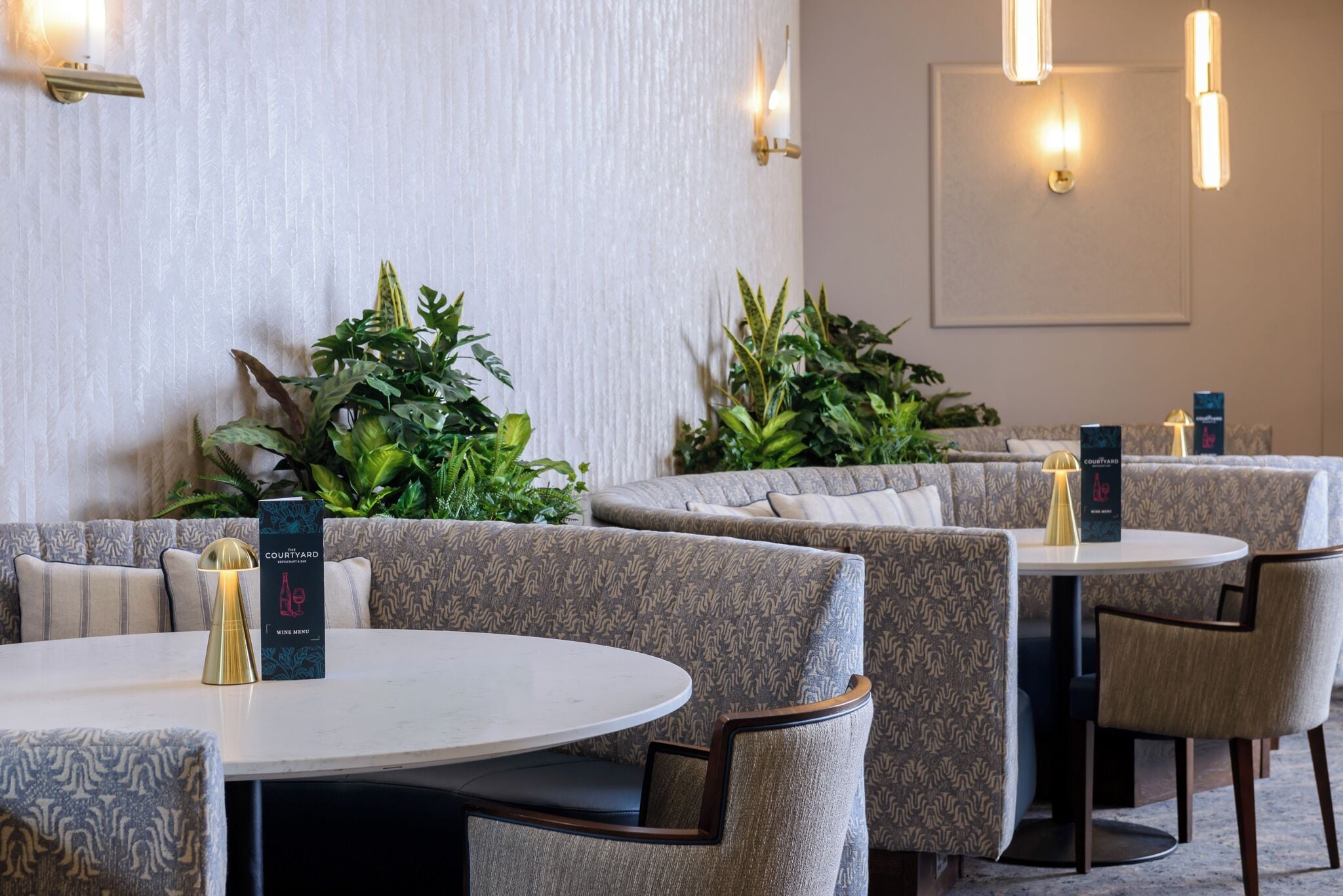 A restaurant with round tables and cushioned seating, a wine menu, and wall-mounted lighting.