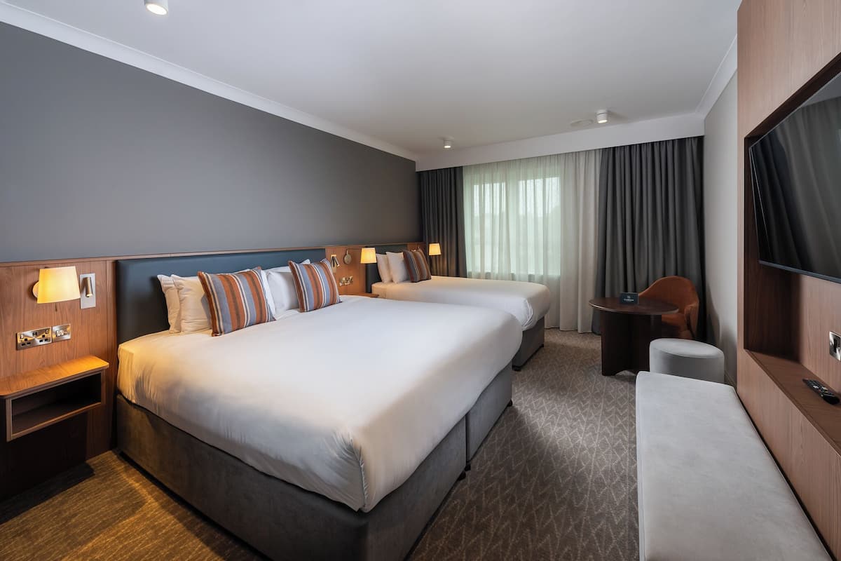 A hotel room with two beds, a desk, a chair, a TV, and a window with curtains.