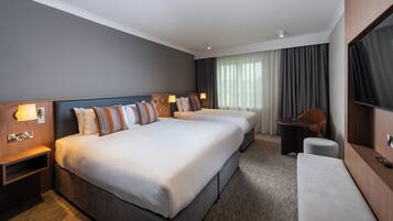 A hotel room with two beds, a desk, a chair, a TV, and a window with curtains.