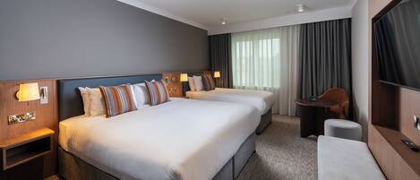 Habitación de hotel con dos camas, un escritorio, una silla, un televisor y una ventana con cortinas.